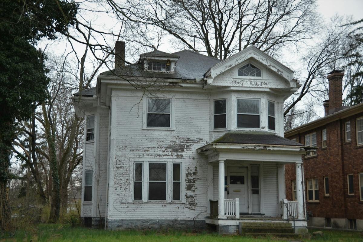 Aging two-story house with peeling paint and a worn front porch, the kind of deferred maintenance that draws code complaints