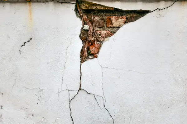 Deep crack running through a plastered wall and exposing the brick underneath, a common sign of foundation movement