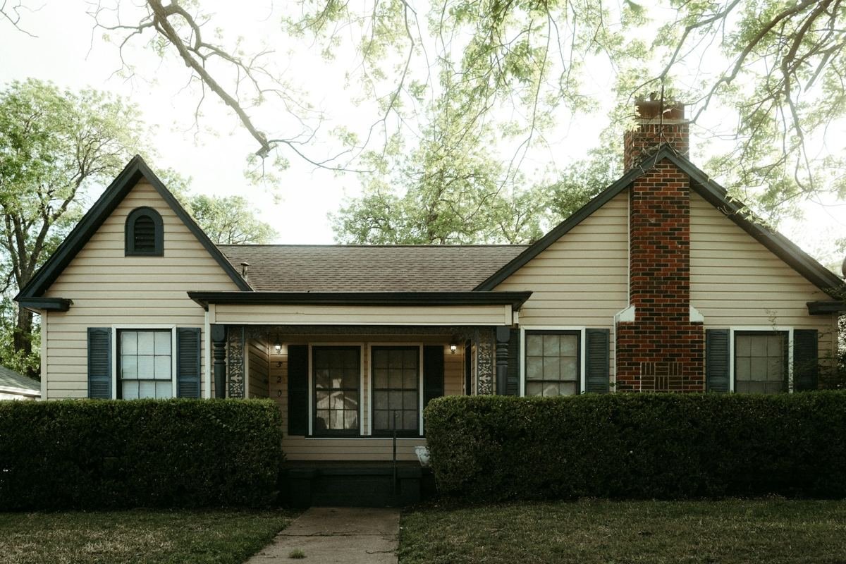 Older single-story family home with a brick chimney, front porch, and mature shade trees