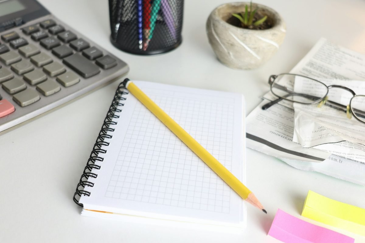 Calculator, spiral notebook, pencil, and reading glasses on a desk, used to add up seller closing costs